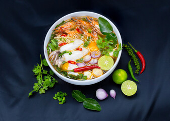 Tom Yum Kung, Thailand favorite spicy boiled food with ingredient are prawn, squid, fish, egg, meat ball and many spicy Thai herb, ready to serve in white bowl on dark background.