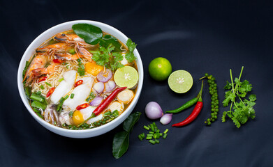 Tom Yum Kung, Thailand favorite spicy boiled food with ingredient are prawn, squid, fish, egg, meat ball and many spicy Thai herb, ready to serve in white bowl on dark background.