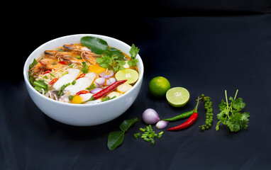 Tom Yum Kung, Thailand favorite spicy boiled food with ingredient are prawn, squid, fish, egg, meat ball and many spicy Thai herb, ready to serve in white bowl on dark background.