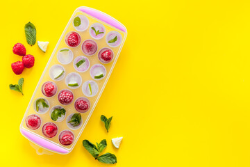 Ice tray with berries, lime and mint on yellow background top view copy space
