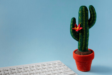 Green blooming cactus toy and white keyboard on a blue background. Home office concept. Learning or...