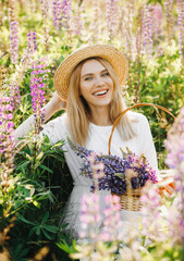 Young blonde with short hair in a summer white dress. Woman poses in a lupine field