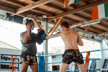Training in the gym in the ring with a muay thai trainer. Tattooed caucasian man and Asian trainer....
