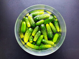 fresh cucumbers soaked in water in a glass dish, on a black background