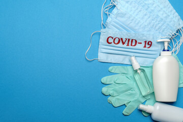 Stack of Disposable blue medical face masks with COVID-19 sign, rubber latex gloves and alcohol hand sanitizer antiseptic on blue background