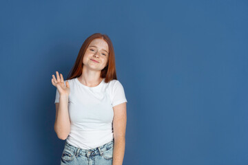 Say hello. Caucasian young girl's portrait on blue background. Beautiful female redhair model with cute freckles. Concept of human emotions, facial expression, sales, ad, youth culture.