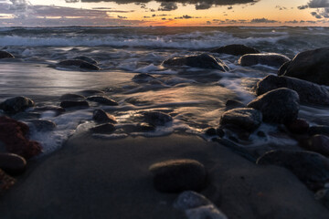 Obraz premium long exposure landscape, rocky ocean coastline with blurry waves in orange sunset light
