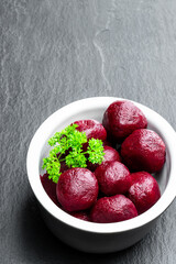 Homemade pickled baby beetroot in clay pot on black stone background