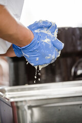 Hand of teenager in blue glove squeezing grated cabbage in pan on wooden white table surface. Cooking stage for coleslaw, fermented cabbage and salad. Background for healthy food and hygiene concept.
