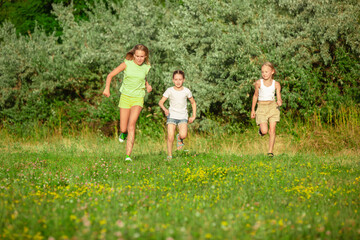 Obraz premium Kids, children running on meadow in summer's sunlight. Look happy, cheerful with sincere bright emotions. Cute caucasian boys and girls. Concept of childhood, happiness, movement, family and summer.