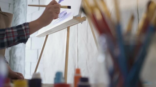 The artist paints on canvas and smears a brush. Canvas stands on the easel.