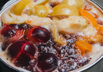 Fruit compote: apricots, plums, apples, cherries are cooked in a metal pan in boiled water with bubbles. Making juice on the stove.