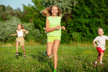 Fototapeta premium Kids, children running on meadow in summer's sunlight. Look happy, cheerful with sincere bright emotions. Cute caucasian boys and girls. Concept of childhood, happiness, movement, family and summer.