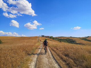 Plakat Ragazzo e gruppi di ragazzi in bicicletta in mezzo ad un campo di grano al cielo azzurro della toscana