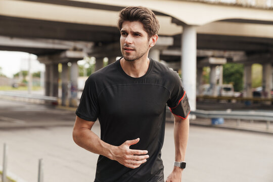 Image of athletic sportsman with smartphone running while working out