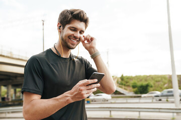 Image of smiling young sportsman using cellphone while working out