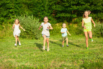 Fototapeta premium Kids, children running on meadow in summer's sunlight. Look happy, cheerful with sincere bright emotions. Cute caucasian boys and girls. Concept of childhood, happiness, movement, family and summer.