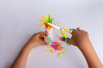 child makes a parrot craft from recycled yogurt bottle, DIY . Kindergarten or school children activity, funny bird craft for kids