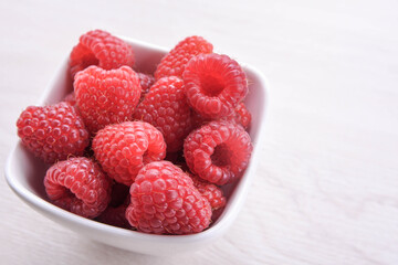 Bowl of fresh raspberries with green leaves on wooden background. Top view