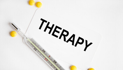 Obraz premium On the card is the inscription THERAPY, next to the thermometer and yellow tablets.