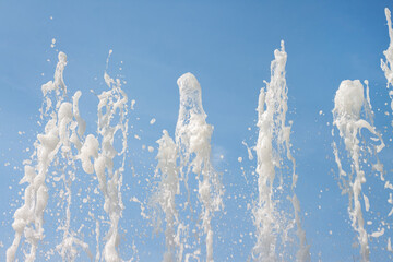 Obraz na płótnie Canvas Flowing fountain water jets spray texture with blue bright sky background refreshing macro wallpaper