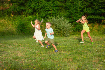 Obraz premium Kids, children running on meadow in summer's sunlight. Look happy, cheerful with sincere bright emotions. Cute caucasian boys and girls. Concept of childhood, happiness, movement, family and summer.