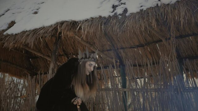A witch with a black crown on his head and a staff in his hands slowly goes limp
