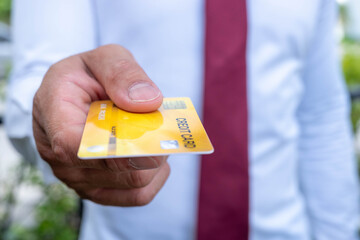 The businessman stands the yellow credit card ahead as he sits at the office desk.