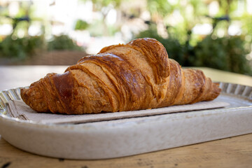 Summer breakfast in vacaton. A beautiful plain french butter croissant on a plat on the outdoor table of a bar in a touristic destination.