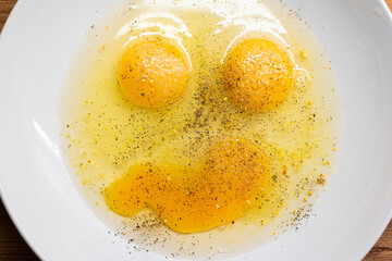 Three whole egg yolks and whites in a soup plate forming an emoji frown y face sprinkled with food spices