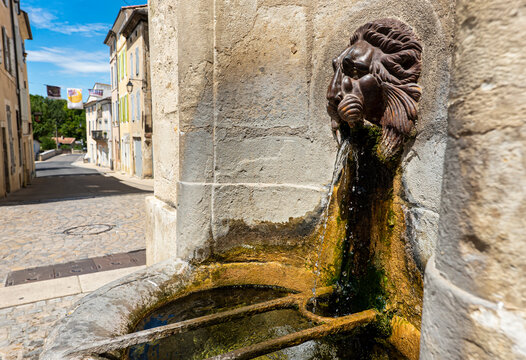 Old lion's head provence style fountain at Dieulefit village with colourful shutters street on the background