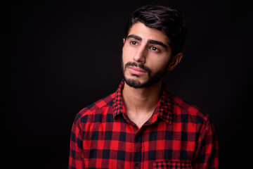 Young handsome bearded Persian man against black background