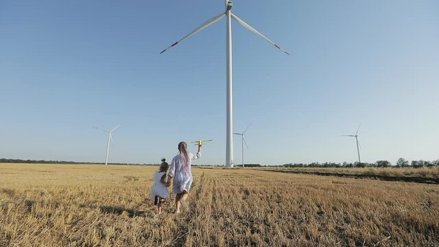 Children play with airplane toy, windmill background. Alternative energy sources concept. 