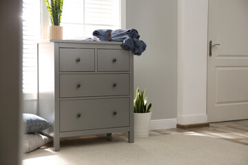 Grey chest of drawers near window in stylish room interior