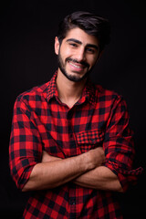 Young handsome bearded Persian man against black background