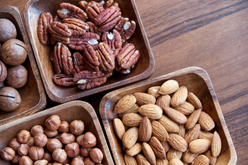 different nuts in small wooden bowl on dark table. Row of bowls with nuts, top view. Peeled nuts. healthy snack concept