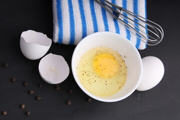 Broken chicken egg sasoned with black pepper. Its ready to be whisked by whisker. Its kept on black background with blue stripped napkin.