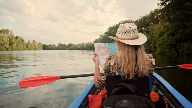 Woman Exploring Calm River By Canoe On Holiday Vacation Weekend.Pretty Woman In Hat Kayaking On Lake At Sunset And Holds Oar.Girl Traveler Swim In Kayak Boat And Looking Map.Girl In Kayak Summer Trip