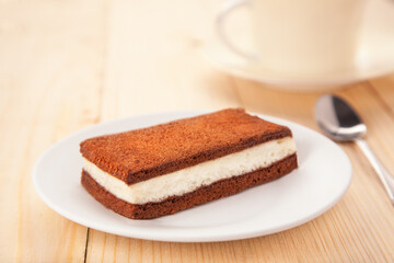 delicious sweet cake dessert with tiramisu cream between two chocolate biscuit on plate on wooden table. Close up view.
