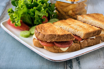 Grilled and pressed toast with turkish sausage, cheese, tomato and lettuce served on white plate.