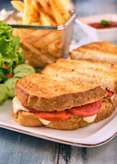 Grilled and pressed toast with turkish sausage, cheese, tomato and lettuce served on white plate.