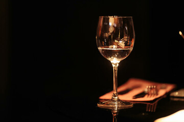 A glass of white wine on a glass table on a black background