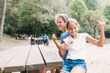 Two funny sisters laughing and singing at the table in a picnic area