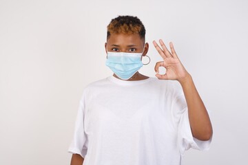 Glad attractive woman shows ok sign with hand as expresses approval, has cheerful expression, being optimistic. Standing against white wall.