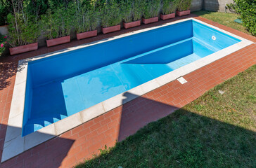 A swimming pool with blue coating in a private garden is completely empty, waiting to be filled with water for the start of the summer season