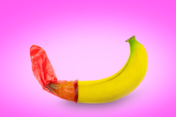 Red condom wear a banana on a pink background concept safe sex prevention of sexually transmitted...