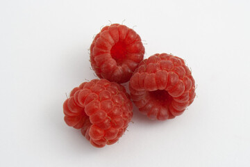 Three ripe raspberries isolated on a white background close-up. Fresh raspberries without sheets on the table. Macro shooting. Healthy and wholesome food concept