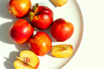 Red ripe organic nectarine fruits on the white plate on nature background. Summertime healthy eating concept. Fruit antioxidant. Selective focus. Top view