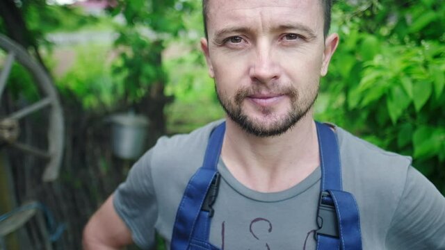 Worker in the garden. Young adult man stands in the summer garden and looks at the camera