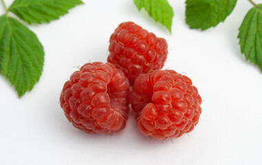 Three ripe raspberries isolated on a white background close-up. Beautiful red fresh raspberry with leaves along the contour on the table. Macro shooting. Healthy and wholesome food concept